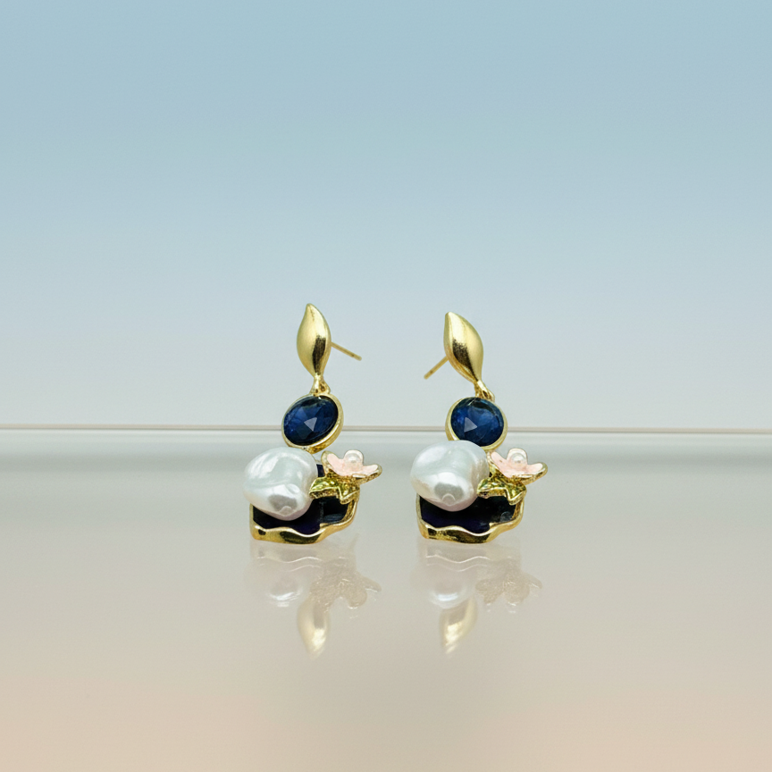Pair of gold earrings with blue stones and pearls on a gradient background, branded 'Mosa Jewellery'.