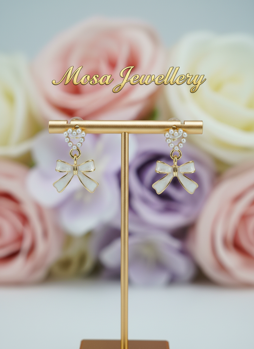 Bow-shaped earrings on a stand with pastel roses in the background, branded 'Mosa Jewellery'.