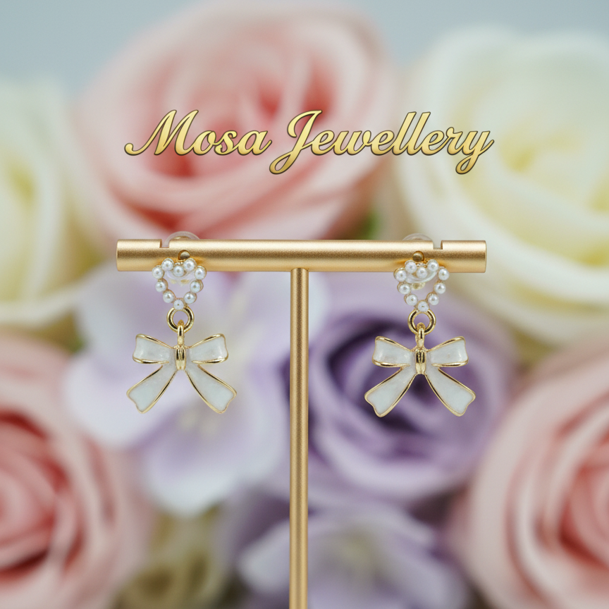 Bow-shaped earrings on a stand with pastel roses in the background, branded 'Mosa Jewellery'.