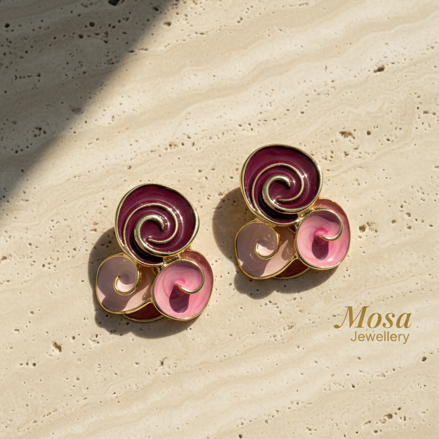 Pair of spiral-shaped earrings with pink and purple colors on a beige stone surface, branded 'Mosa Jewellery'.