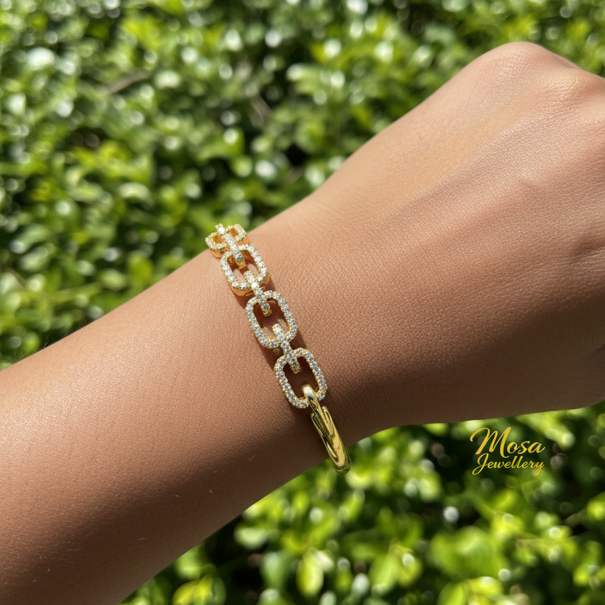 Gold chain bracelet on a wrist with a blurred green background