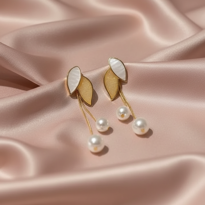 Gold and pearl earrings on a pink satin background