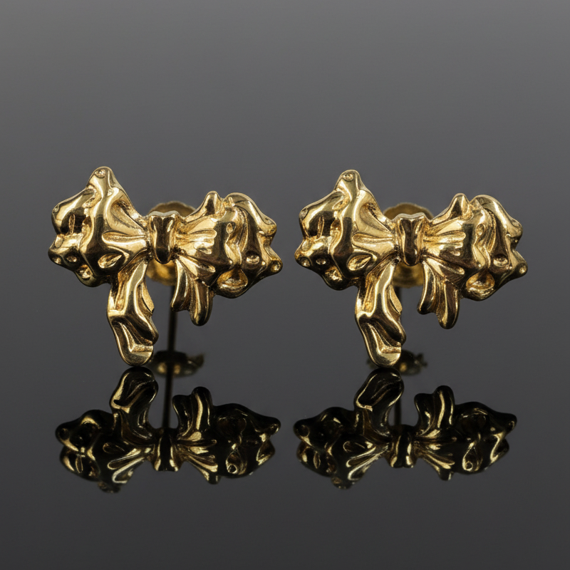 Pair of gold bow-shaped earrings on a reflective surface with a gray background